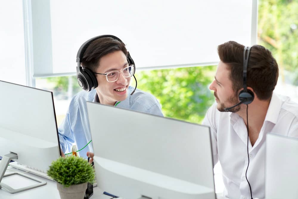 Male customer support service operators with headsets talking at light office