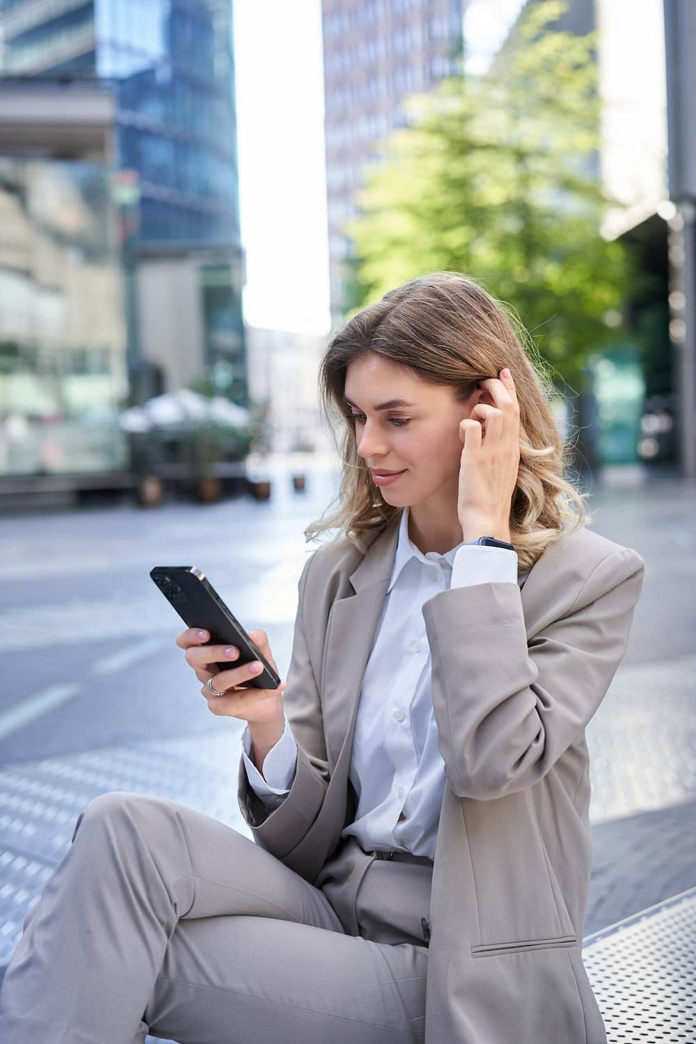 Vertical portrait of woman in suit using mobile phone, reading message or checking app, posing